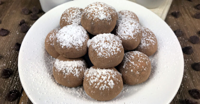 Stack of chocolate truffles covered in powdered sugar on a white plate.