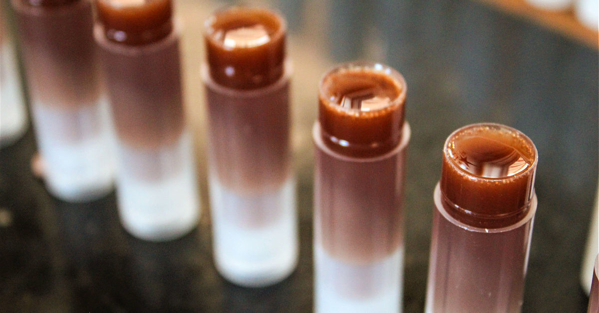 Lip balm tubes being filled with melted chocolate lip balm mixture.