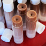 Three open tubes of chocolate lip balm on a red tray with more closed tubes.