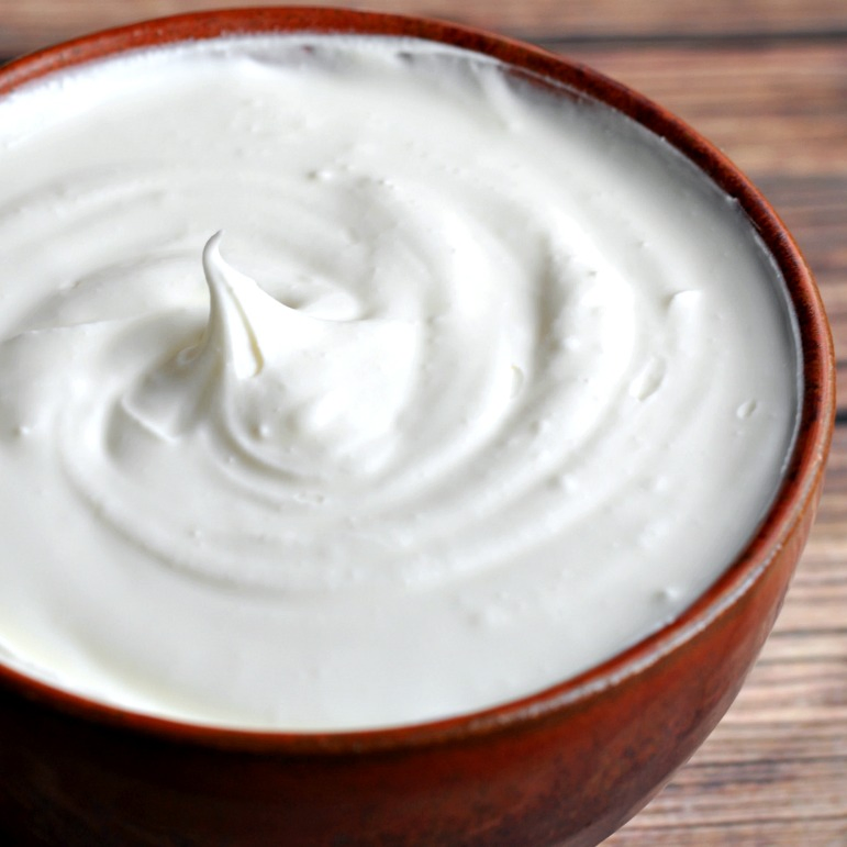 Close up of bowl of homemade sour cream on wood table