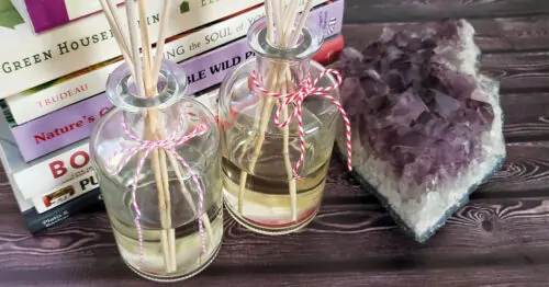 Two homemade reed diffusers next to a stack of books and amethyst crystal.