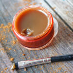 Honey cinnamon lip gloss and lip brush on wood table.