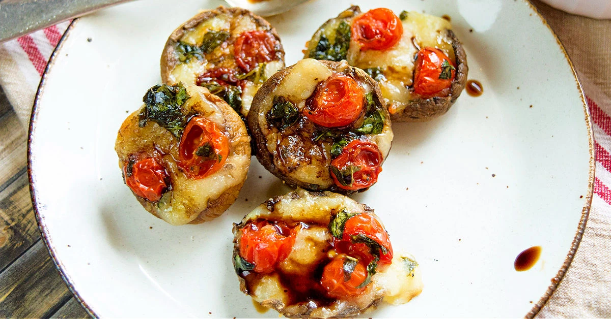 Plate of Caprese stuffed mushrooms appetizer drizzled with balsamic vinegar.