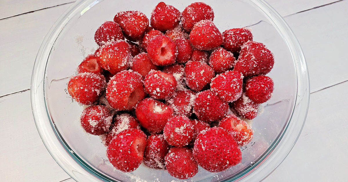 Fresh strawberries coated in granulated sugar in a large mixing bowl.