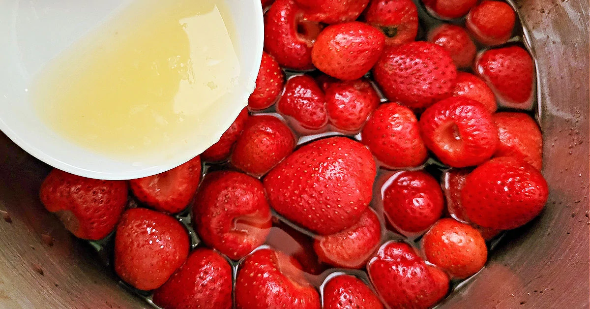Fresh lemon juice being added to boiling strawberries in a large stockpot.