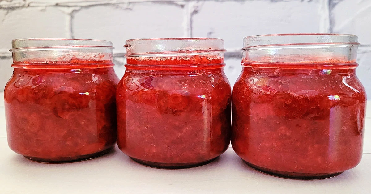Three 8-ounce glass jars of strawberry jam without lids on them.