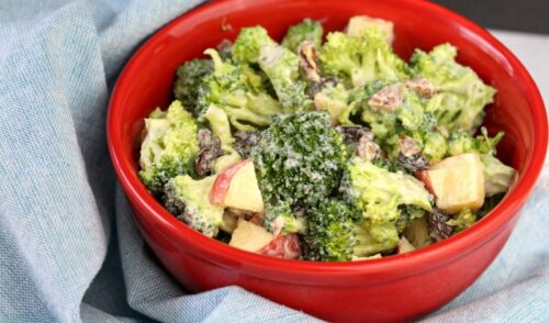Red bowl of homemade broccoli salad on light blue towel