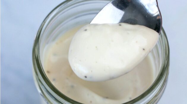 Greek yogurt dressing for broccoli salad being taken out of a jar jar with a silver spoon