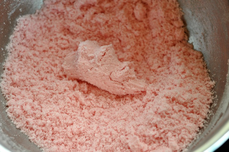 Pink bath bomb mixture in a bowl pressed together to test its readiness to mold