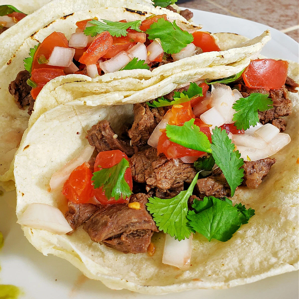 Close up carne asada street tacos that were prepared in an Instant Pot, topped with homemade pico de gallo
