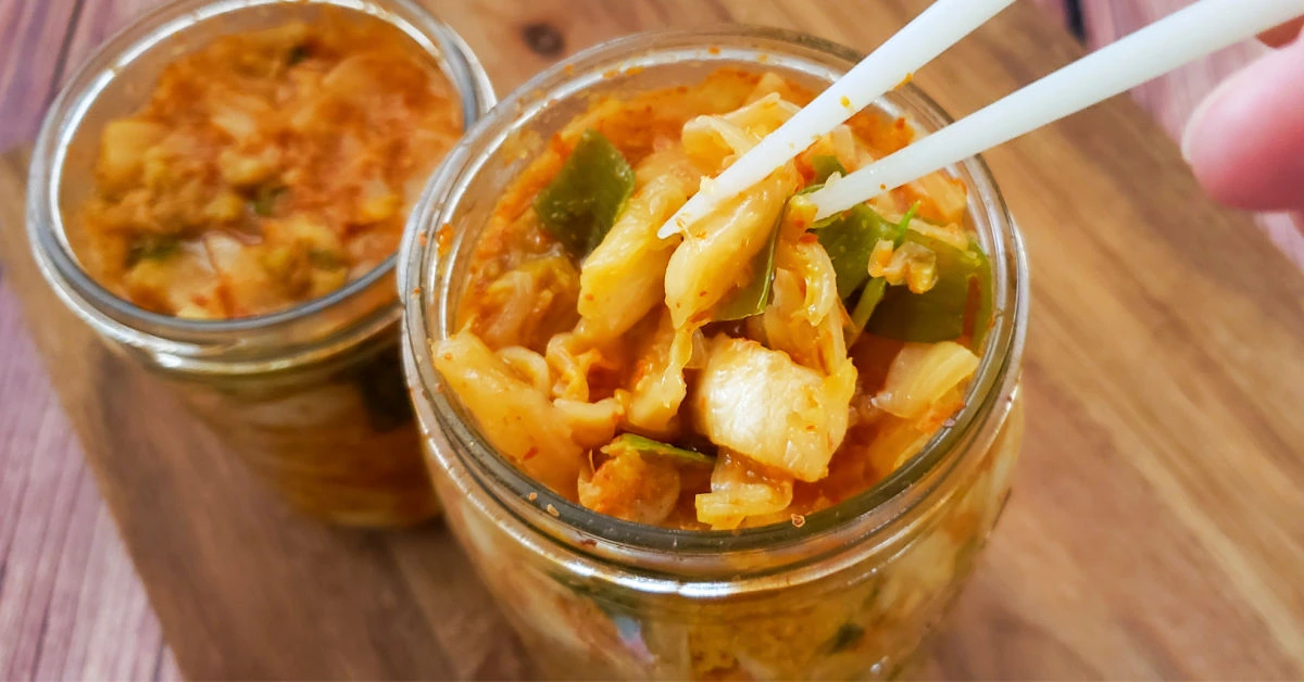 Kimchi being removed from a mason jar with a pair of chopsticks.