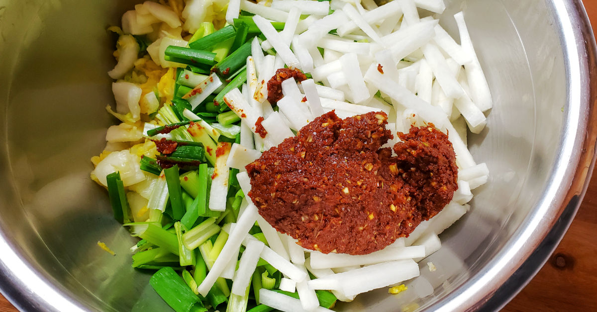Napa cabbage, green onions, daikon radish and kimchi chili paste in mixing bowl.