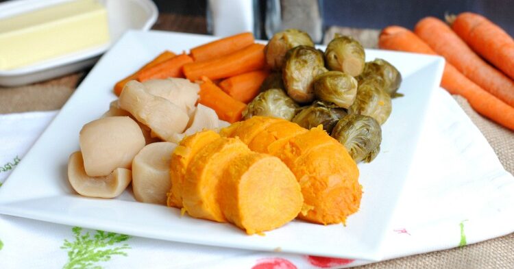 White plate of vegetables on table with raw carrots, butter, salt and pepper