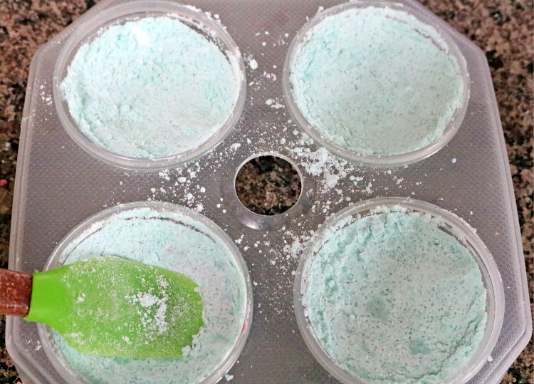 Headache bath bomb mixture being pressed into a bath bomb mold with a green silicone spatula