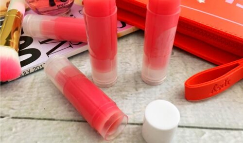 Close up of tubes of mica tinted lip balm on a white wood table