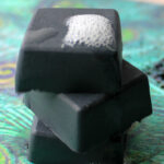 Close up of 3 stacked and lathered charcoal soap bar squares