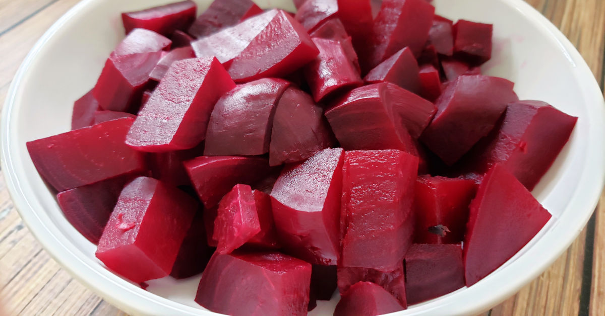 Poached red beets in a white serving bowl.