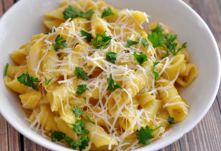 Butternut squash sauce over gluten free pasta topped with parmesan and parsley in a white bowl