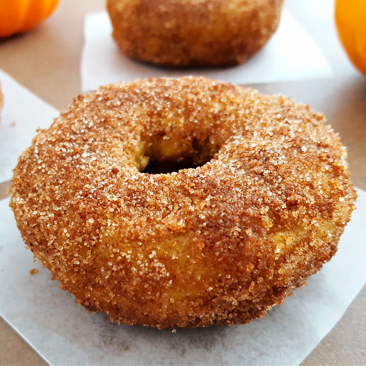 Pumpkin Snickerdoodle gluten free donut on a parchment paper square on a brown table