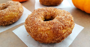 Gluten Free Pumpkin donut coated in cinnamon sugar on a square of parchment paper square.