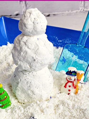 Sensory bin filled with homemade fake snow, tree and snowman figurines, blue plastic scoop and small snowman made from the fake snow.