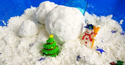 Fake snow in a sensory bin with a small pine tree and snowman figurine.