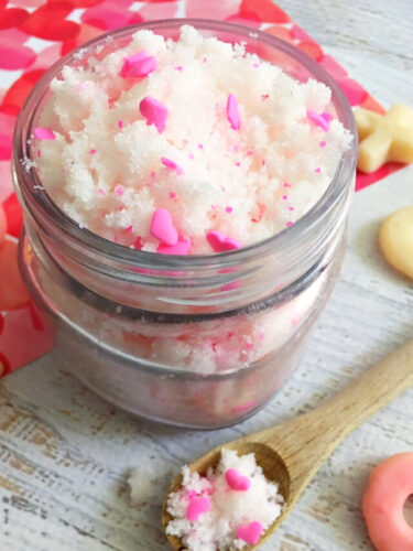 White sugar scrub with pink hearts in a glass jar on a white wood table with heart tissue paper