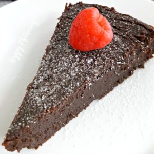 Slice of gluten free flourless chocolate torte topped with a raspberry