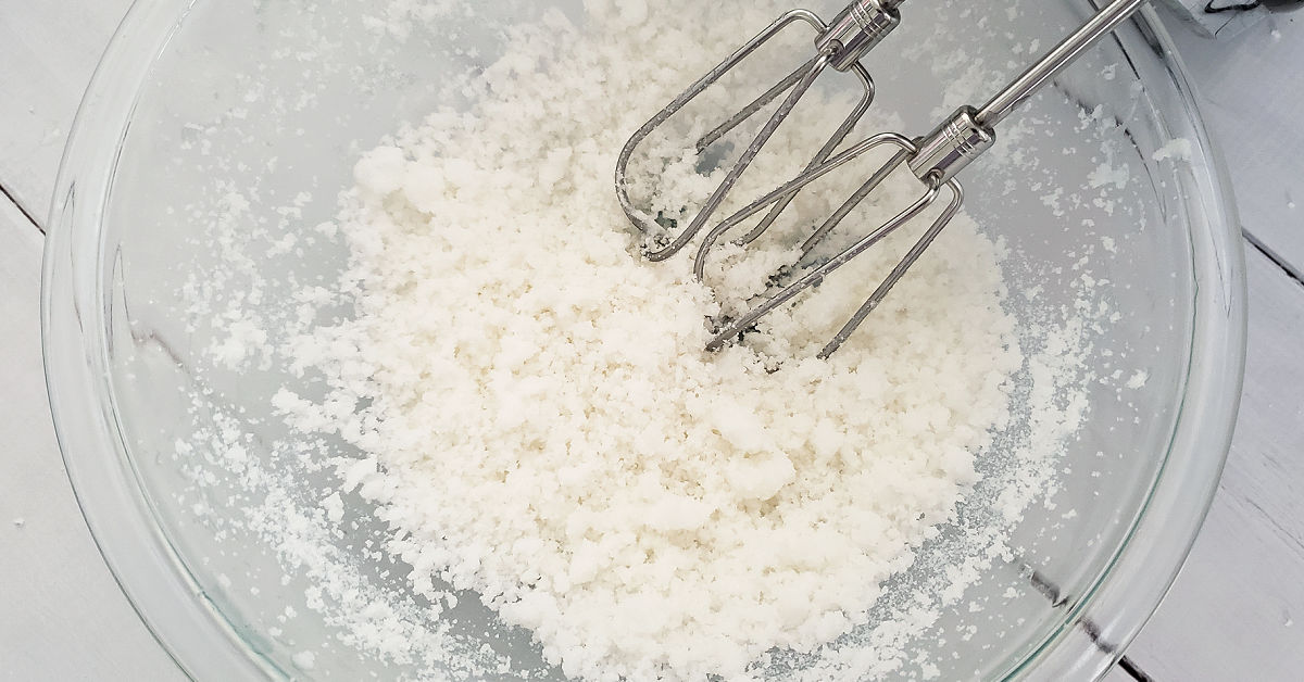 Sugar and coconut oil being whipped together with a hand mixer.