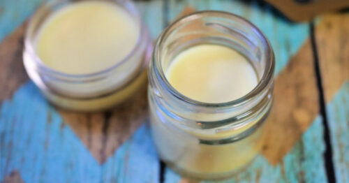 Two glass jars of homemade sore muscle relief balm on a table