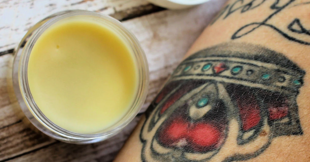 A tub of homemade tattoo balm on the table next to a tattooed arm with vibrant colors.