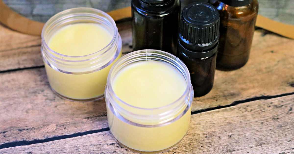 Two tubs of homemade antihistamine balm on table with 3 essential oil bottles.