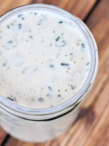 Homemade ranch dressing in a pint sized glass mason jar sitting on a brown table, cropped into a square