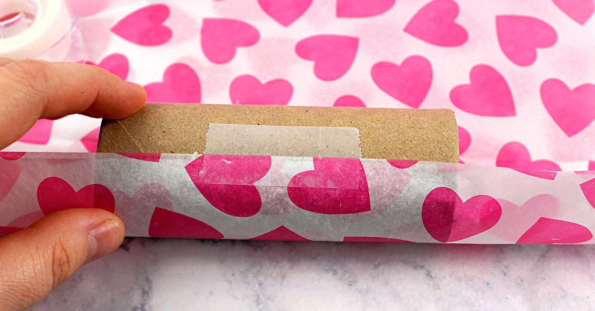 Heart print tissue paper being taped onto a toilet paper roll.