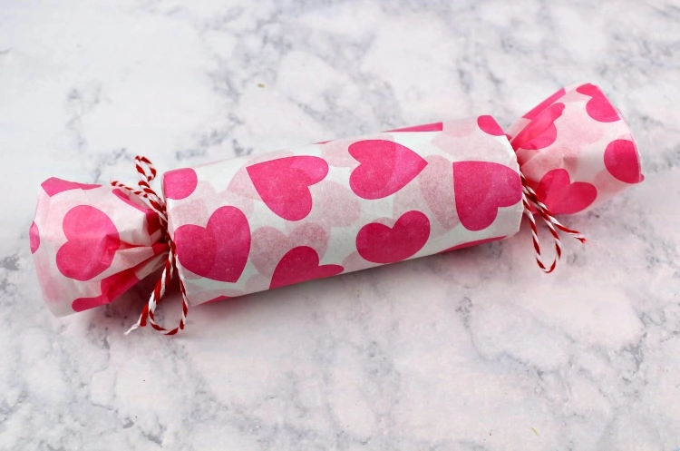 Toilet paper tube filled with candy and toys, covered in heart print tissue paper and tied closed with baker's twine.