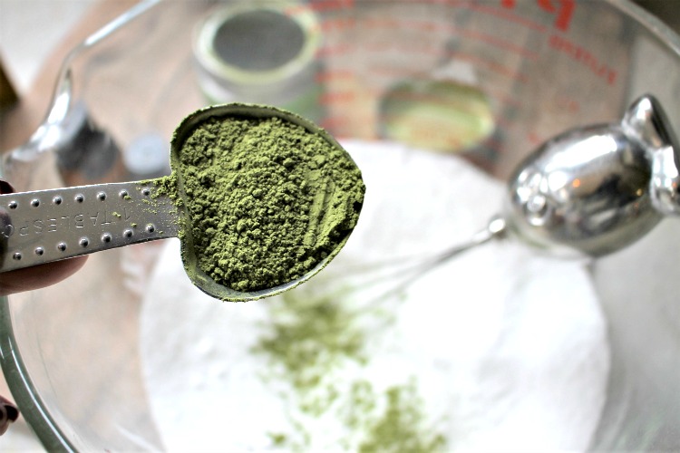 Matcha green tea being added to baking soda and epsom salts in a bowl