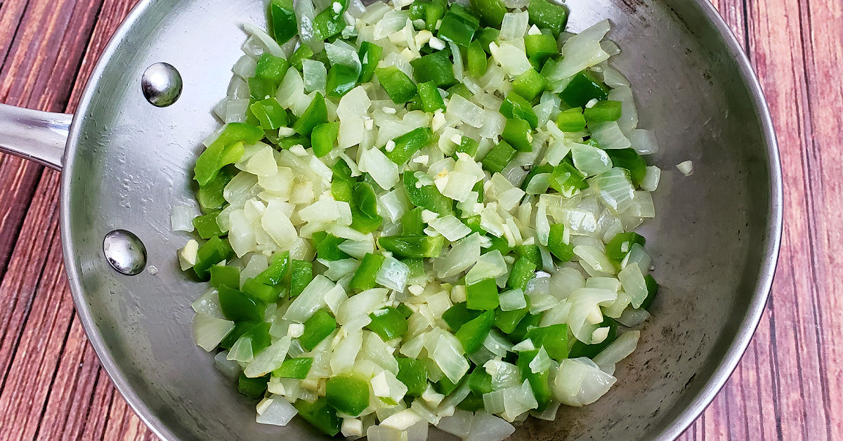 Sauteed green bell pepper, onion and garlic in a small stainless steel frying pan.