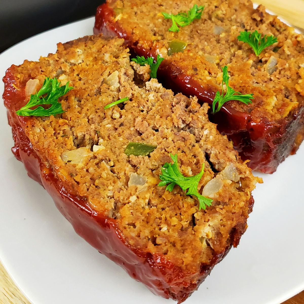 Close up of two slices of gluten free meatloaf topped with chopped parsley on a white plate.