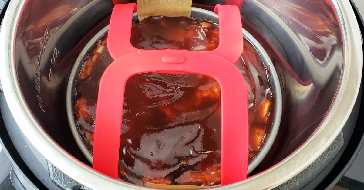 Meatloaf mixture in cake pan lowered into Instant Pot inner pan with red silicone sling.