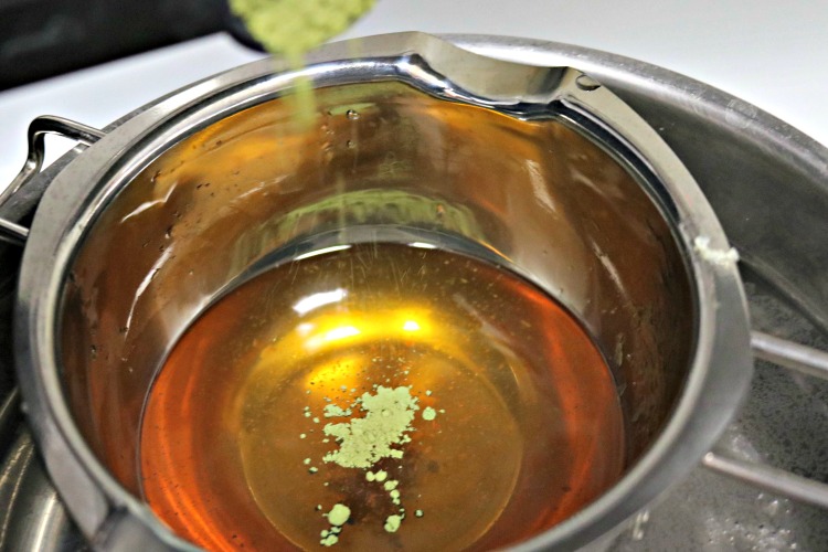 Matcha green tea powder being added to the double boiler to make a green tea salve.