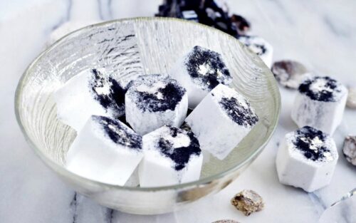 Clear decorative glass bowl on a marble counter filled with charcoal bath bombs with more spilling onto the counter