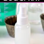 Clear spray bottle filled with homemade essential oil bug spray with measuring cups behind it on the counter