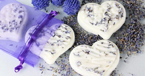 Homemade lavender lotion bars spilling out of a purple organza bag on a white table.