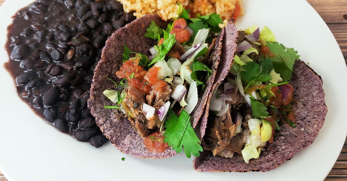 Barbacoa beef served in blue corn tortillas, topped with salsa, cilantro and onion and served with with black beans and Spanish rice.