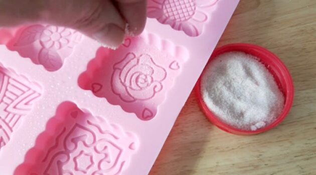 Sea salt being sprinkled into the bottom of a pink silicone mold