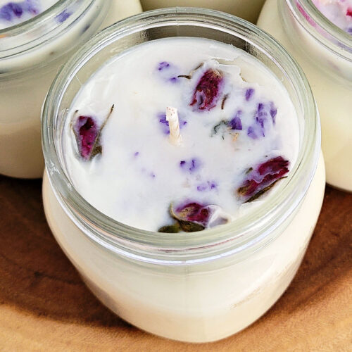 Closeup view of a homemade soy candle with dried flowers on wood slice.