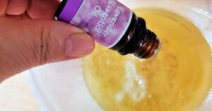 Lavender essential oils being added to wax and oil in bowl.