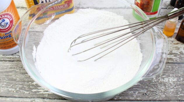 Dry ingredients for shower steamers added to a glass mixing bowl with a whisk