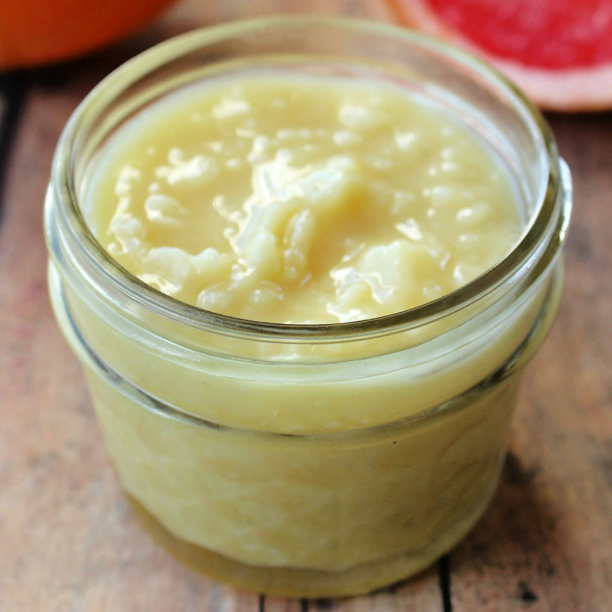 DIY cellulite cream in a clear glass mason jar on a brown table with a slice of grapefruit behind it