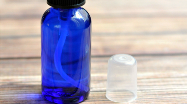 Close up of blue spray bottle of face toner with cap sitting next to it on wood table